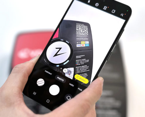 Gros plan d'une main tenant un smartphone devant une borne de recharge laissant apparaitre un code QR sur l'écran du téléphone