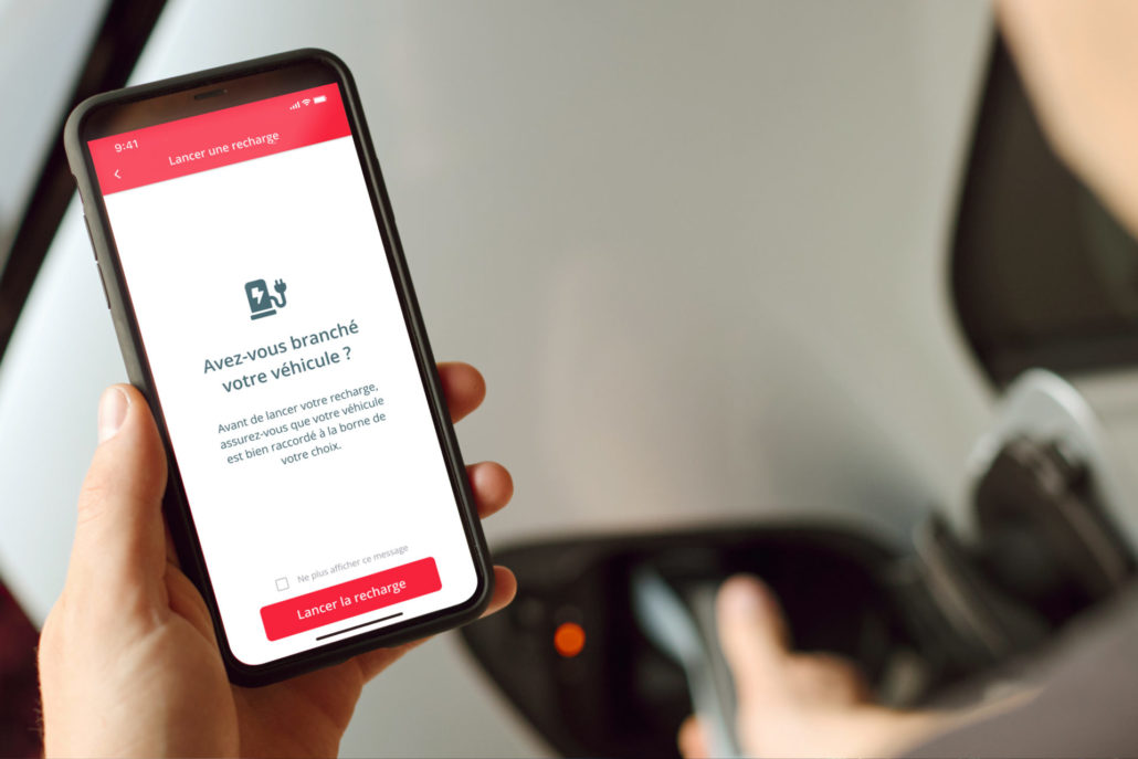 Un gros plan d'un homme vu de dos regardant son smartphone avec la fonction App Start de volta affichée, lui permettant de lancer la recharge de son véhicule électrique directement depuis son téléphone