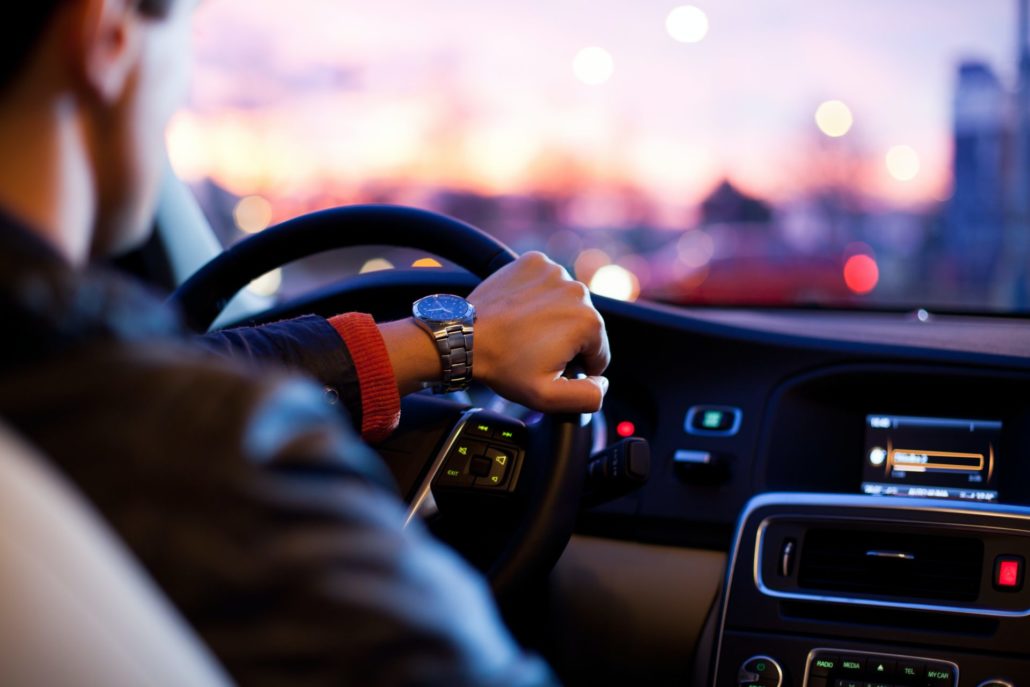 Un homme vu de dos au volant de son véhicule électrique avec au loins les lumières de la villes en flou