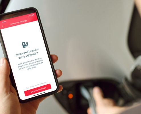 Un gros plan d'un homme vu de dos regardant son smartphone avec la fonction App Start de volta affichée, lui permettant de lancer la recharge de son véhicule électrique directement depuis son téléphone